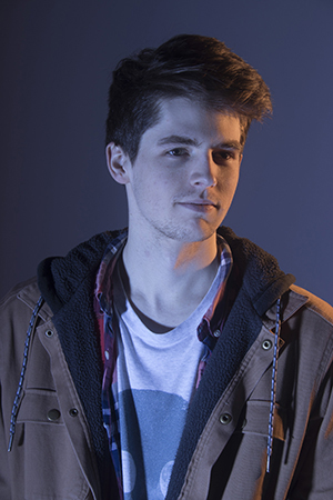 Austin Meros’s shoulders face forward, gaze to the forward right, lit dramatically, close mouth, subtle smile