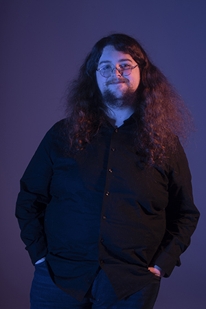 With a small smile, Brian's hands are in his pockets and he stands facing the camera.