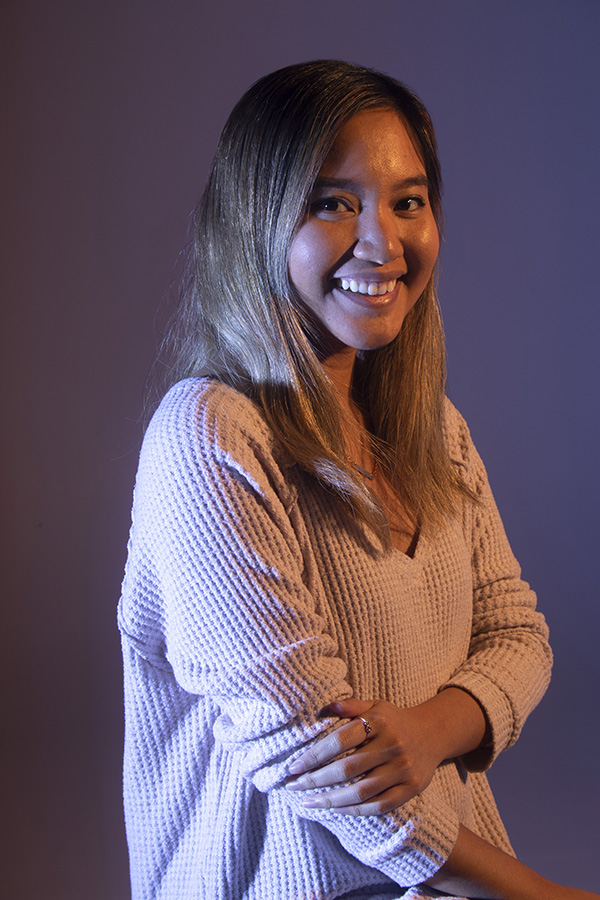 Dramatically-lit photograph of julie with shoulders turned to right, head turned to camera smiling, right arm across body holding left arm