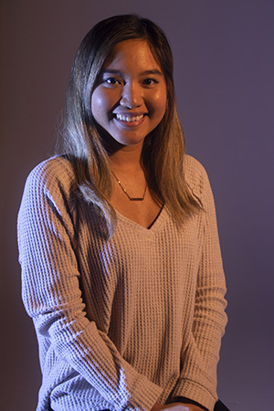 Dramatically-lit photograph of Julie sitting, smiling at camera, hands crossed at lap