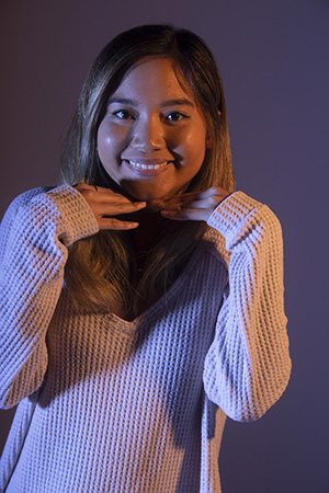 Dramatically-lit photograph of Julie, smiling at camera, chin resting on hands