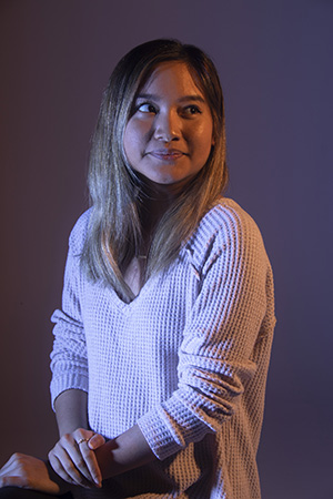 Dramatically-lit photograph of Julie sitting with shoulders facing left, gaze right, hands crossed at lap