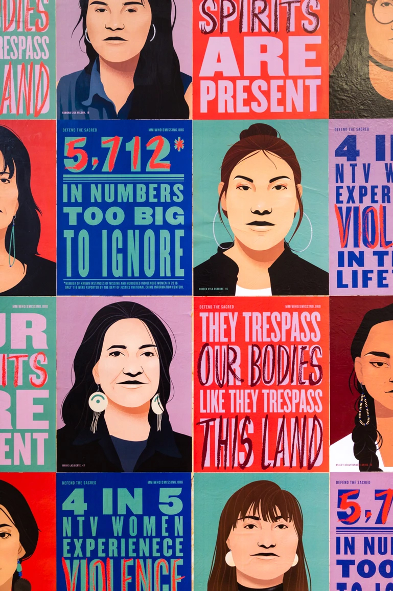 Photograph of wheat pasted posters of graphic illustrated portraits of missing indigenous women and calls to action for justice, in a checkered grid
