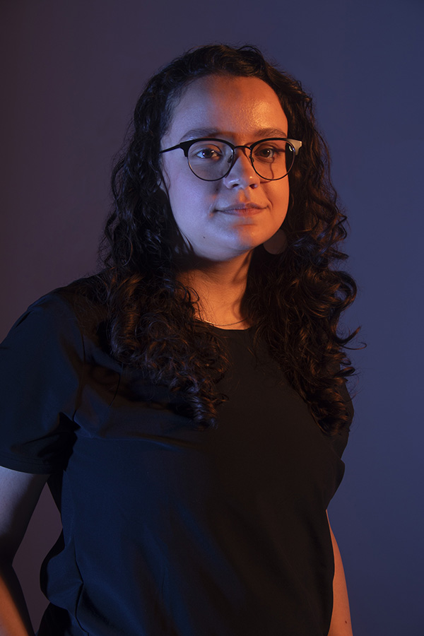 Kalila looks at the camera with slight smile, dramatic lighting, arms to the side