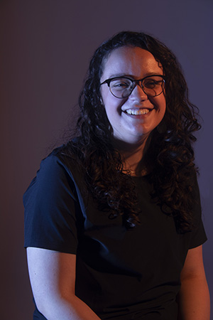 Kalila laughs with eyes closed facing camera, dramatic lighting, hands on lap