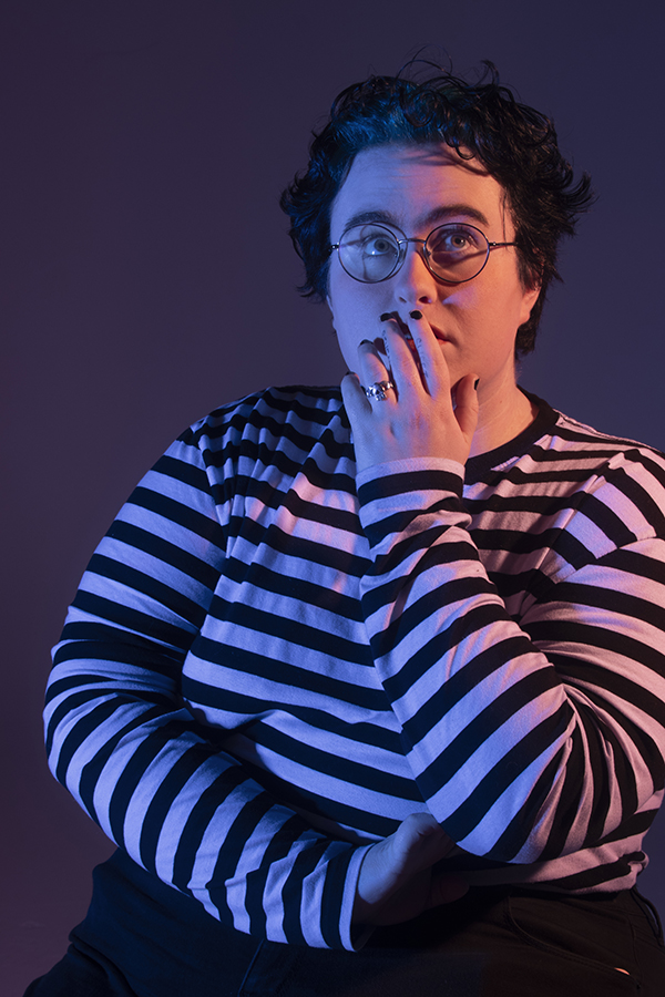 KD sits in dramatic lighting, gazing upward quizically, left hand gently covering mouth