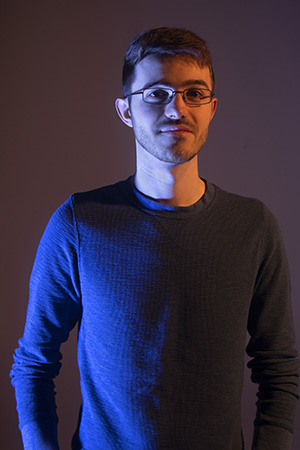 Kent stands in dramatic lighting, gaze slight to the right, shoulders squared to the center, arms to the side