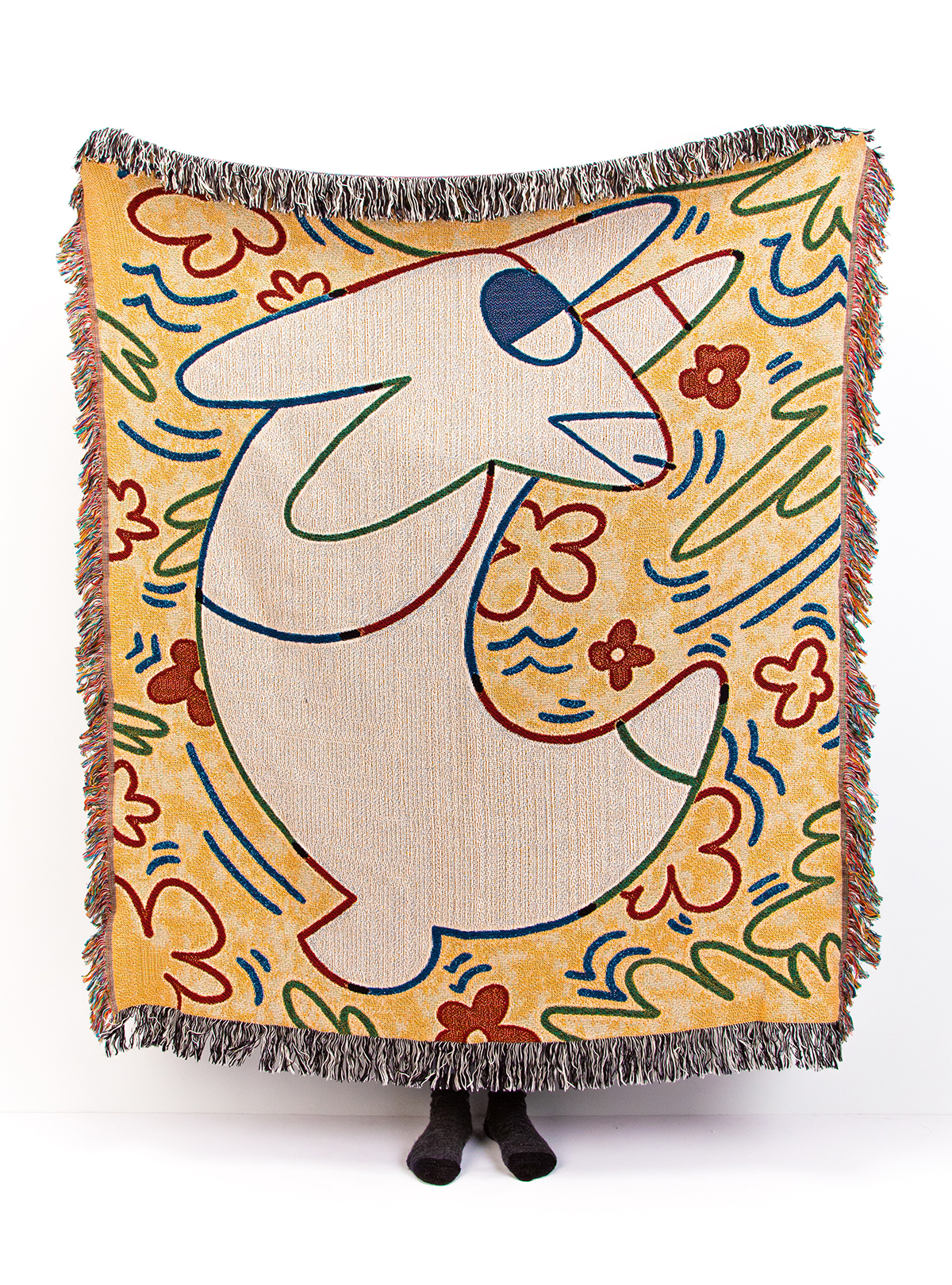 Lauren holds up a large throw quilt with an illustrated pattern of one large white rabbit and flowers