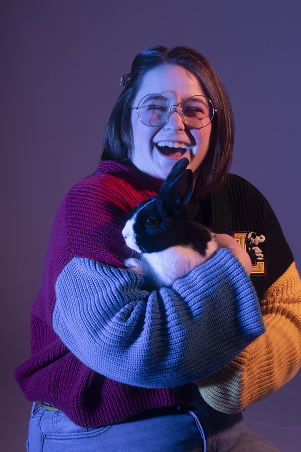 Lauren sits in dramatic lighting, laughing at the camera holding a black and white pet bunny