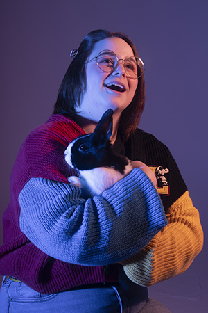 Lauren sits in dramatic lighting gazing to the upper right hugging a pet black and white bunny