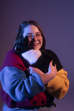 Lauren sits in dramatic lighting snuggling a pet black and white bunny to shoulder