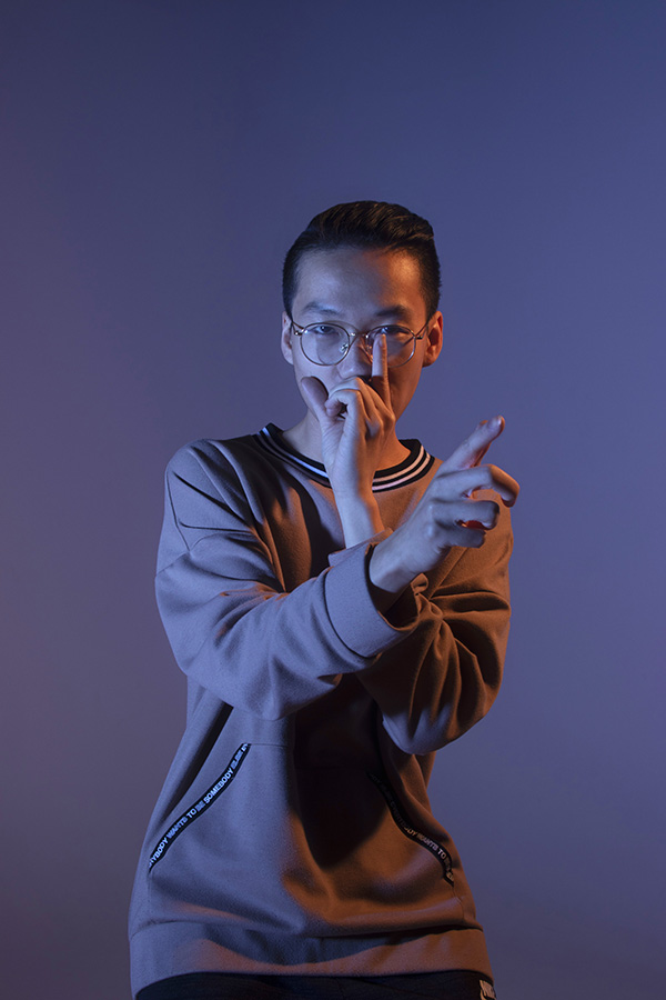 Trung photographed in dramatic lighting while beatboxing, one hand raised in front of his lips and the other pointing in front of him as he moves.